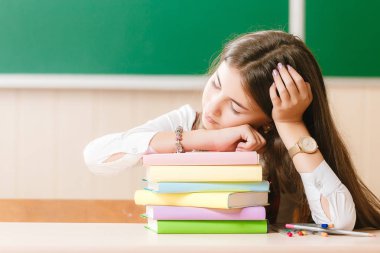 Öğrenci üniforma okulda ders sırasında kitaplar üzerinde uyuyor. sınıfta onun masasında oturan kız.