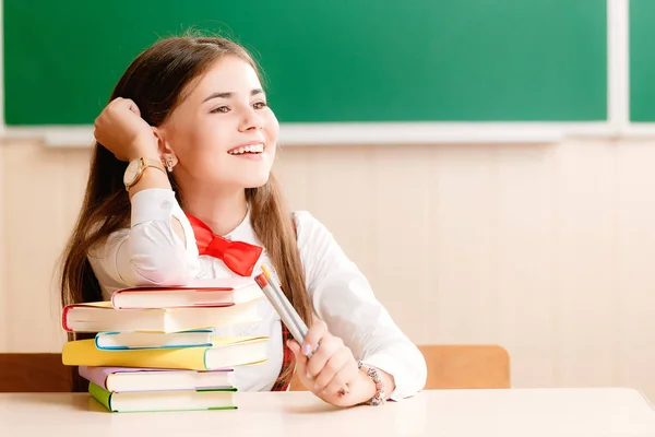 Дівчина в шкільній формі сидить за своїм столом у класі з книгами. Студент в класі в школі — стокове фото