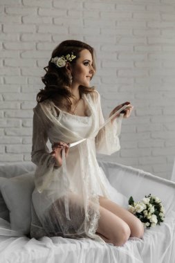 Pencerenin yanındaki parlak odada sarı saçlı güzel bir kız. Bir buket ile sabahlık Gelin