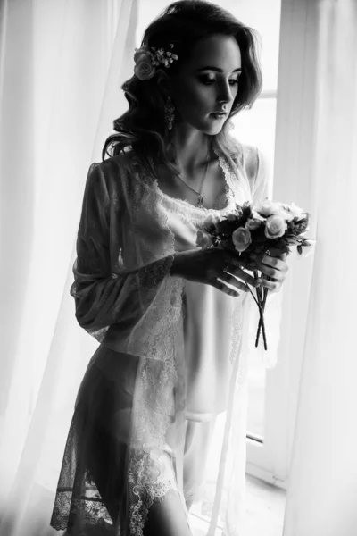 Menina bonita com cabelo loiro em um quarto brilhante perto da janela. Noiva em vestido de vestir com um buquê — Fotografia de Stock