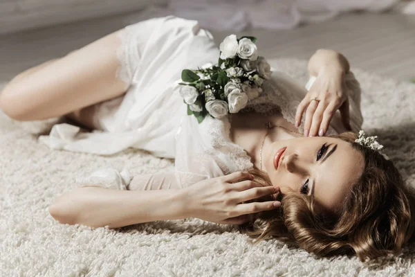 Gadis cantik dengan rambut pirang di ruangan yang cerah berbaring di lantai. Pengantin berbaring memegang karangan bunga — Stok Foto