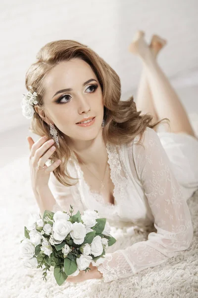 Krásná dívka se světlými vlasy v jasné místnosti leží na podlaze. Nevěsta ležící v ruce kytice — Stock fotografie