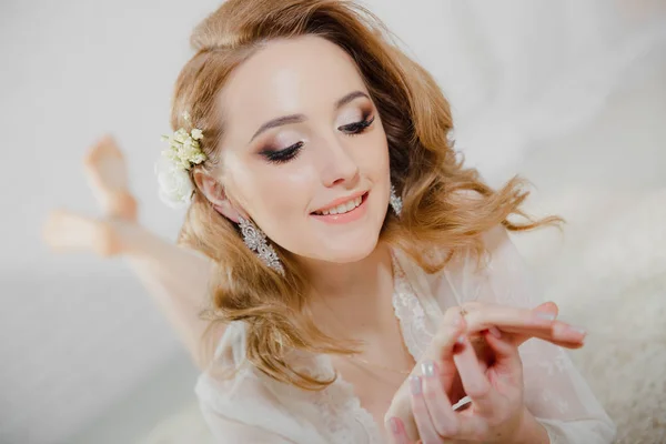 Bella ragazza con i capelli biondi è sdraiata sul pavimento. La sposa è sdraiata a guardare la sua fede nuziale e sorridere . — Foto Stock