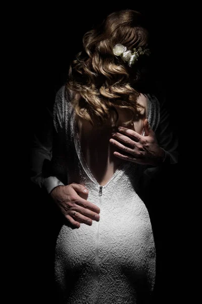 gelin ve damat arkada. Bir adam beyaz elbiseli bir kıza sarılır. Damadın elleri ve gelinin arkası.