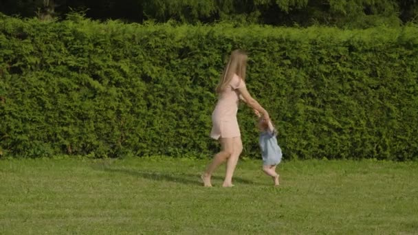 女婴和妈妈在公园的夏日灯光下玩绿草 宝宝玩得开心点母亲和女婴旋转的缓慢动作 快乐的家庭理念 长的头发的妇女 — 图库视频影像