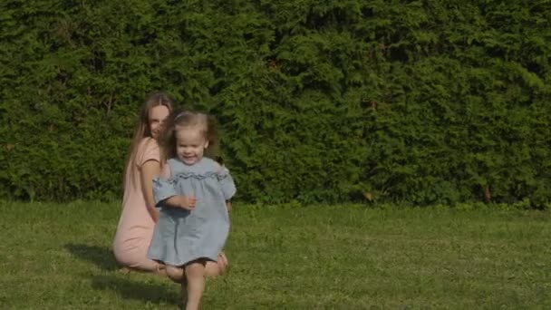 女婴逃离妈妈 在公园的夏日灯光下微笑 慢动作 绿草背景 快乐的家庭理念 宝宝玩得开心点长的头发的妇女 — 图库视频影像