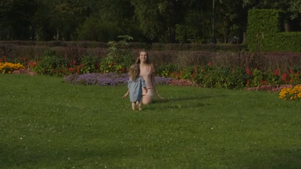 在公园的夏日灯光下 女婴和妈妈在绿草上玩红球 宝宝玩得开心点彩色夏季花卉背景 快乐的家庭概念 — 图库视频影像