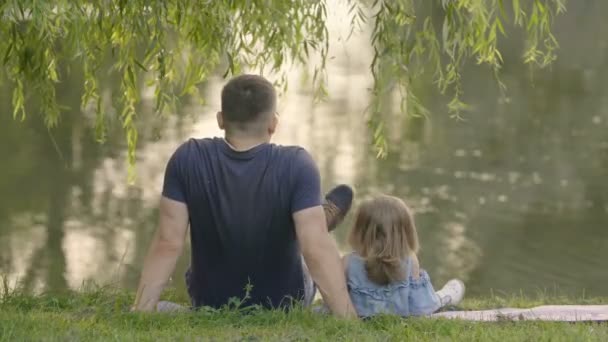 Figlia Piccola Con Padre Seduto Sotto Albero Vicino Lago Abbraccio — Video Stock