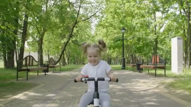 女の赤ちゃんは公園で自転車に乗ります 笑顔と笑いの幸せな子供 小さな女の子が自転車に乗って市の公共公園 — ストック動画