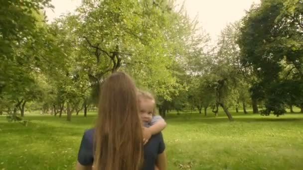 年轻的母亲背着一个疲惫的婴儿户外在夕阳的阳光下平静疲惫的女婴 慢动作 从背面拍摄 — 图库视频影像