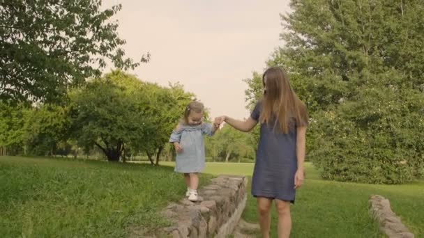 在公园的夏日灯光下 带着妈妈的女婴走在石道上 妈妈帮女儿走石头走道 宝贝玩得开心 慢动作 幸福家庭理念 — 图库视频影像