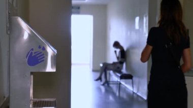 Temassız dezenfektan hastane koridorunda duruyor. Bir kız antiseptiğin yanından geçiyor..