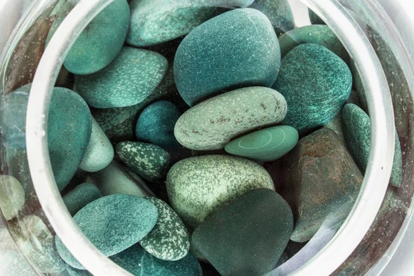 sea stones turquoise in water in a glass vase from above on a white background