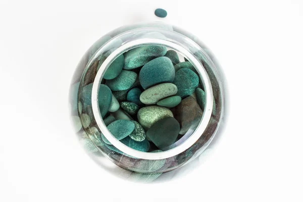 Piedras de mar turquesa en agua en un jarrón de cristal desde arriba sobre un fondo blanco Imagen De Stock