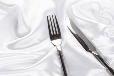 Beyaz ipek masa örtüsü üzerinde çatal ve bıçak. Romantik bir akşam yemeği. Üst görünüm.