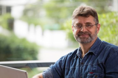 İhtiyar bir adamın gülümseyen portresi vardır gülümseyen ve hapy yeşil arka planda.