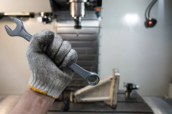 The hand of a mechanic is holding a wrench for repairing the machine.