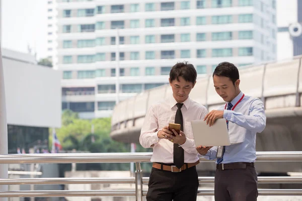 Dos hombres de negocios están trabajando codo a codo con un teléfono inteligente y sin él. Imagen de archivo