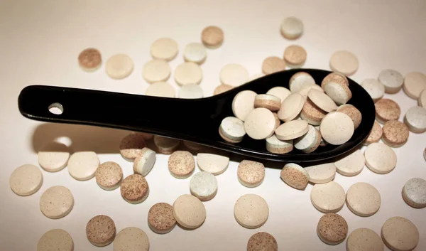Pillole farmaceutiche in cucchiaio di ceramica nera su sfondo chiaro . — Foto Stock