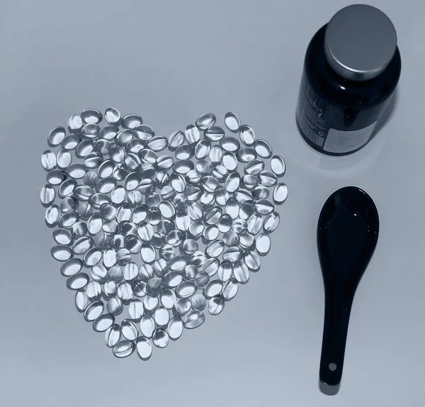 A black spoon, dark bottle and Omega-3 lying in the shape of a heart on white background. — Stock Photo, Image