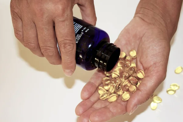 Yetişkin kadın kıdemli omega 3, yakın çekim şişe el Sarı kapsül dışarı dökülen.
