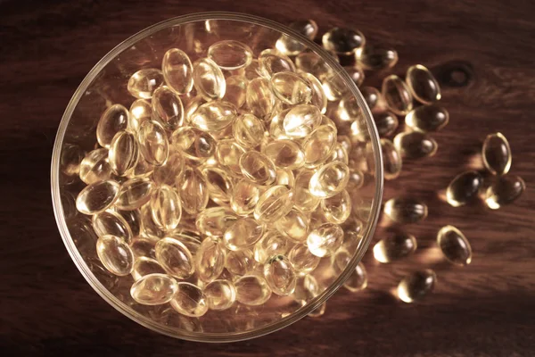 透明黄色药丸在木背景的玻璃碗, 胶囊鳕鱼肝油, 欧米茄3. — 图库照片