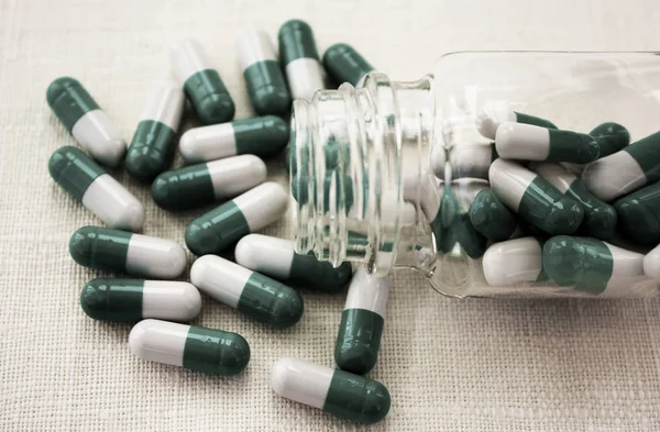 Capsule bianche di colore verde fuoriuscita dal flacone di medicinale trasparente, dalle pillole e dal flaconcino distesi su sfondo bianco . — Foto Stock