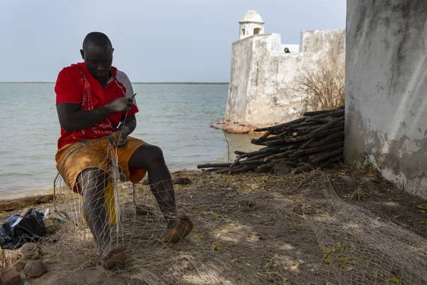 Cacheu, Republic of Guinea-Bissau - February 1, 2018: Fishermen repairing fishing nets next to the Cacheu Fortress in the city of Cacheu, in Guinea Bissau. — Stock Image Cacheu Republic Guinea Bissau February 2018 Fishermen Repairing Fishing Nets Royalty Free Stock Images