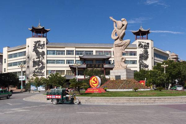 Dunhuang, China - August 7, 2012: Street scene in the city of Dunhuang, with a roundabout with a statue of an Apsara playing a pipa and the Chinese Communist Party symbol. Dunhuang is a city on the Gansu Province and one of the oasis cities along the