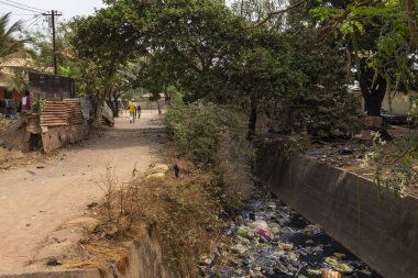 Bissau, Gine Cumhuriyeti - 5 Şubat 2018: Bandim mahalle, bir açık hava kanalizasyon boyunca yürüyen insanlar Bissau şehir. Sağlık ve sağlık koşulları çok kötü Gine Bissau