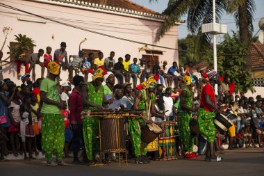 Bissau, Republic of Guinea-Bissau - February 12, 2018: Group of men playing music and wearing costumes during the Carnival Celebrations in the city of Bisssau. clipart