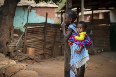 Bissau, Republic of Guinea-Bissau - February 6, 2018: Young girl carrying her baby sister on her back at the Missira neighborhood in the city of Bissau, Guinea Bissau clipart