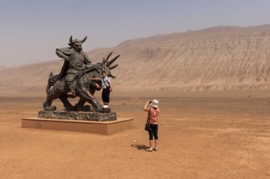 Flaming Mountains, Xinjiang, China - August 12, 2012: Chinese tourists taking pictures in front of a statue near the Flaming Mountains, Xinjiang, China clipart