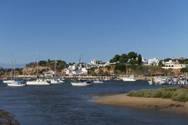 Alvor, Portekiz - 17 Ağustos 2020: Alvor şehrinin beyaz binaları, kilisesi ve limandaki tekneleri, Algarve, Portekiz