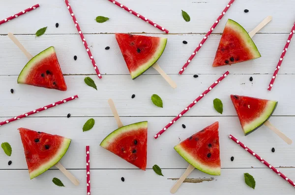 Platt låg bakgrund vattenmelon röd skiva popsicles ordnade med juice halm och mynta blad på vit rustik trä bakgrund. Glad sommar tid flatlay — Stockfoto