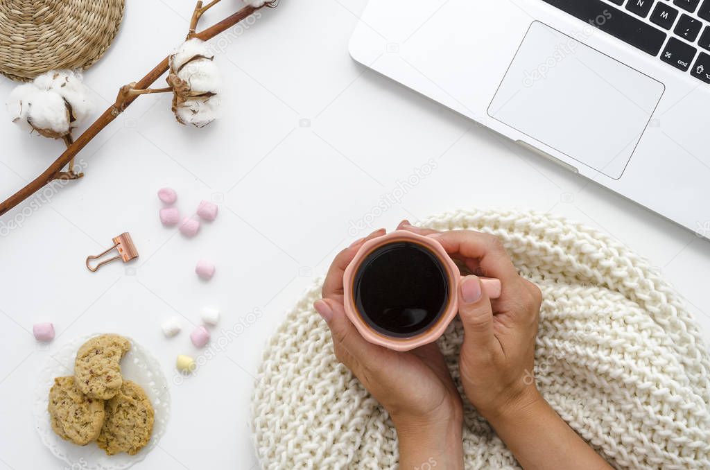 Top view office desk. Girl is holding coffee,workspace is decorated with cotton flowers, computer, marshmallow and oatmeal cookies. Autumn or Winter concept. Flat lay, top view