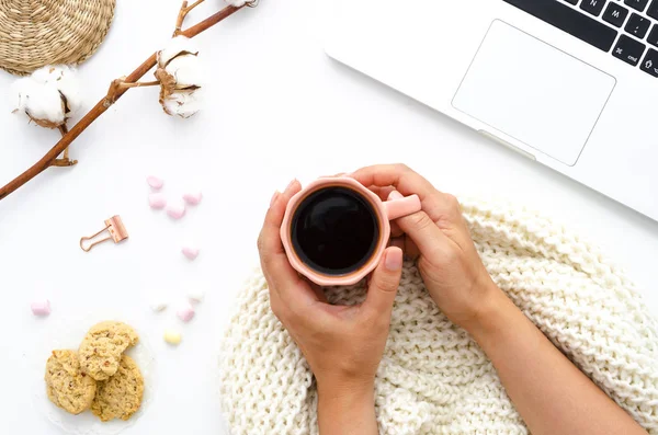 Flicka med en kaffe i hennes händer. Havremjöl kakor, laptop och godis. En bra start på en vinterdag. Bomull blommor dekorera bordet. Höst eller vinter koncept. Platt lekmanna, top view — Stockfoto