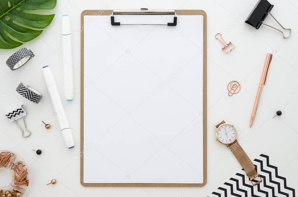 Home office desk with clip board mockup, glasses, golden stationery, green leaves and color markers for drawing. Workspace mock up arranged. Flat lay, top view
