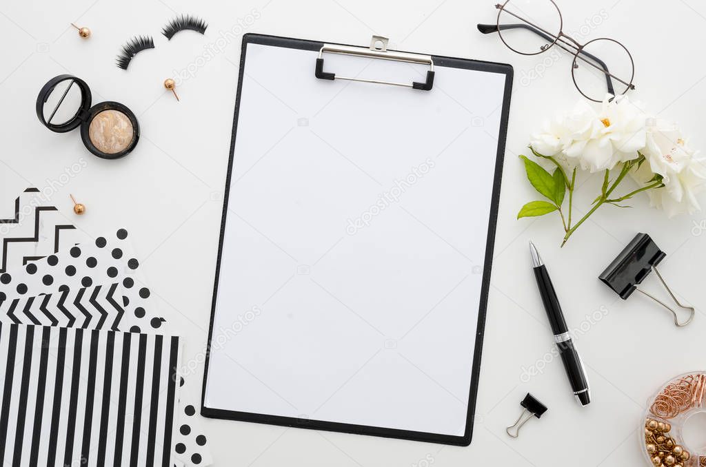 Home office desk with clip board, glasses, white rose, cosmetics, paper clips, eyelashes, and beauty accessories on a white background. Mockup flat lay top view