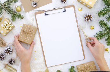 Noel kompozisyon Pano mockup, yeşil ağaç dalları, koni ve craft kağıt üzerinde beyaz bir arka plan ile. Makas ve hediye kutusu elinde tutan kız hediyeler, hazırlama. Düz yatıyordu