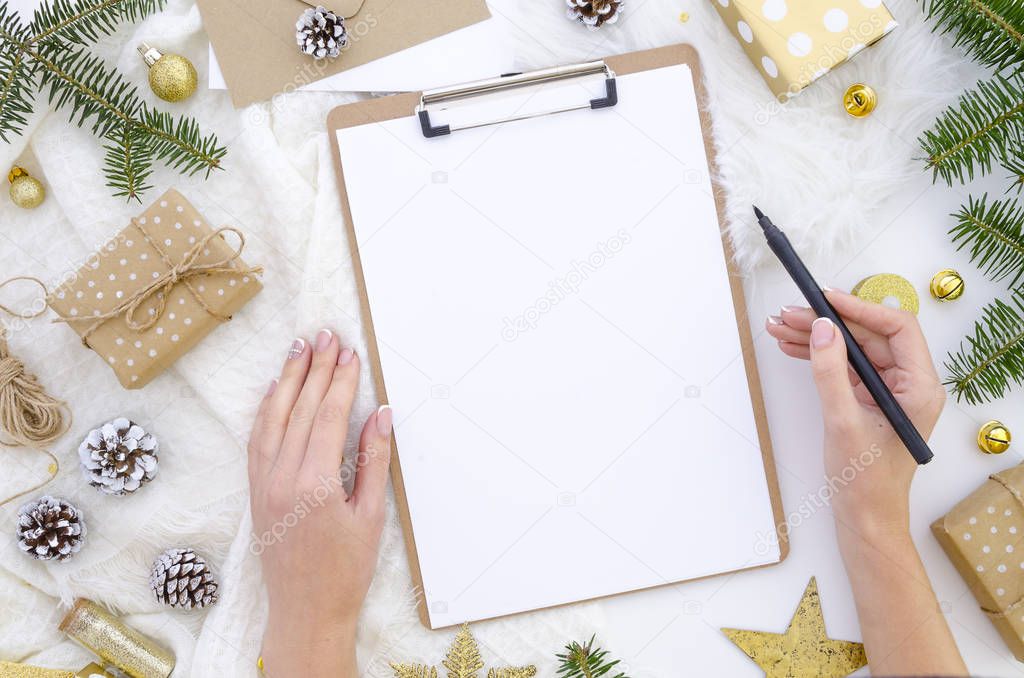 Flat lay christmas clipboard mockup. Womans hands holds black brush pen. Blank white paper sheet clip board mock up. Winter holidays mood for hand lettering. Merry christmas happy new year. Flatlay