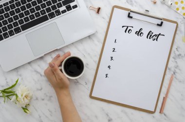 Ofis işleri düz yatıyordu. Yapılacaklar listesi klibi kurulu yazma kız. Bilgisayar, malzemeleri, kahve ve beyaz güller mermer zemin üzerine fincan. Kahve molası, fikirler, notlar, gol veya planı yazma kavramı. Üstten görünüm