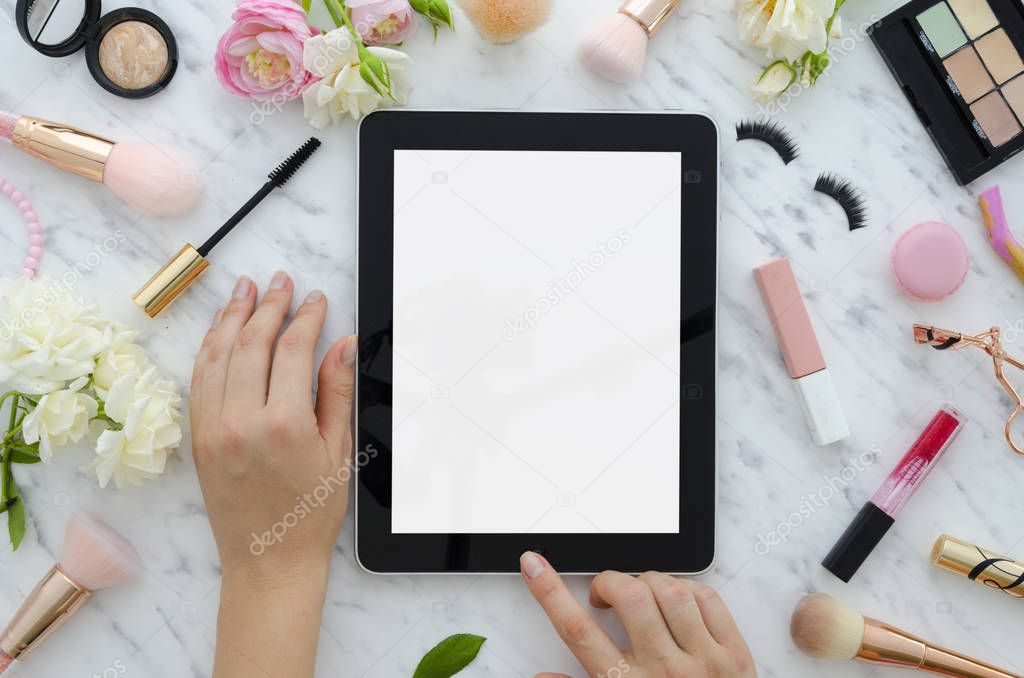 Flat lay of womans glamour beauty products and accessories on a white background. Tablet, brushes, false eyelashes, lipstick, rose macaroons, flowers. Copy space for text. Top view mockup