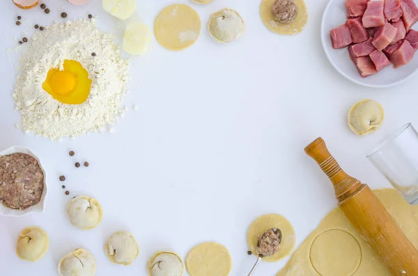 Bolinhos crus na mesa branca. Comida caseira tradicional. O processo de cozinhar bolinhos. Pierogi, pelmeni, ravioli com carne. Moinho de pimenta, pimenta, cebola, carne, ovo. Flat lay, mockup, cabeçalho herói — Fotografia de Stock