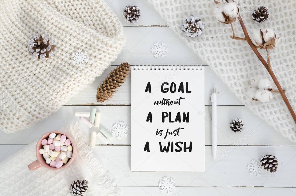 New year motivation a goal without a plan is just a wish. Christmas decorations, knitted blanket, pine cones,cotton flower, marshmello on wooden white background. Flat lay, top view, quote