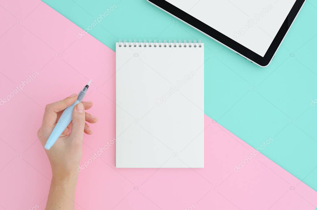 Woman hand writing with brush pen in notepad Top view of tablet on blue and pink two colour vibrant duotone background. Mock up design