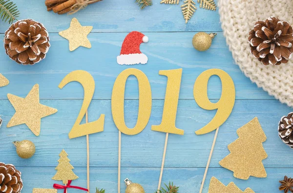 Letras de oro 2019 sobre fondo de tabla de madera azul con conos de pino y bufanda de punto, tarjeta de felicitación de año nuevo 2019, pancarta, vista superior — Foto de Stock