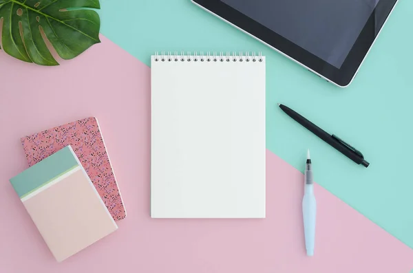 Espaço de trabalho elegante escritório minimalista com tablet, com notebook mock up em branco, lápis, escova, isolado no fundo de cor rosa e azul duotone split. Flat lay estilo vista superior . — Fotografia de Stock