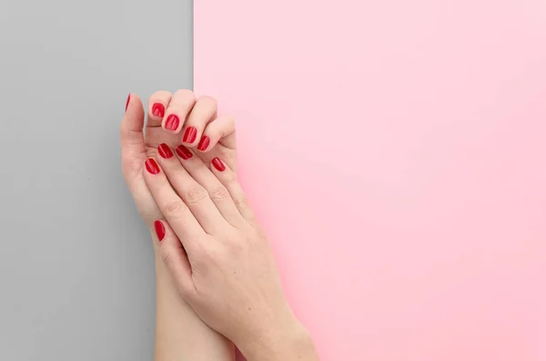 Foto de cerca de unas hermosas manos femeninas con uñas rojas sobre fondo gris y rosa de color duotono partido brillante. Piso de moda. Hermosa maqueta de manicura — Foto de Stock