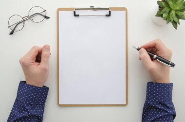 Pano ekli boş beyaz levha ile. Adam ellerini tutar kalem yeşil bitki ve gözlük ile beyaz arka plan üzerinde. Düz yatıyordu mockup iş belge kavramı